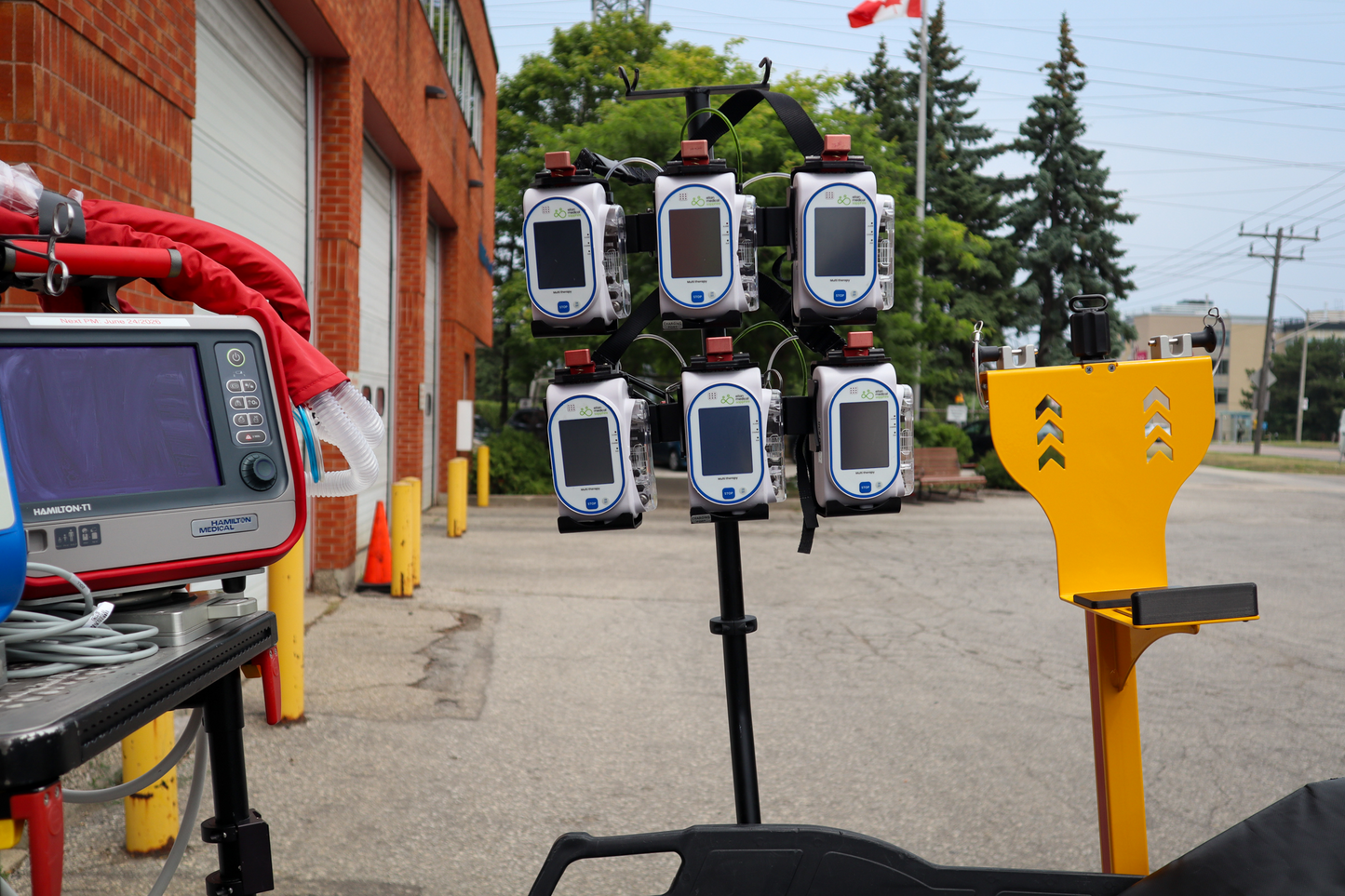 Multiple Sapphire pumps on a Rowland Emergency critical care pole, outdoors with a building and trees in the background.