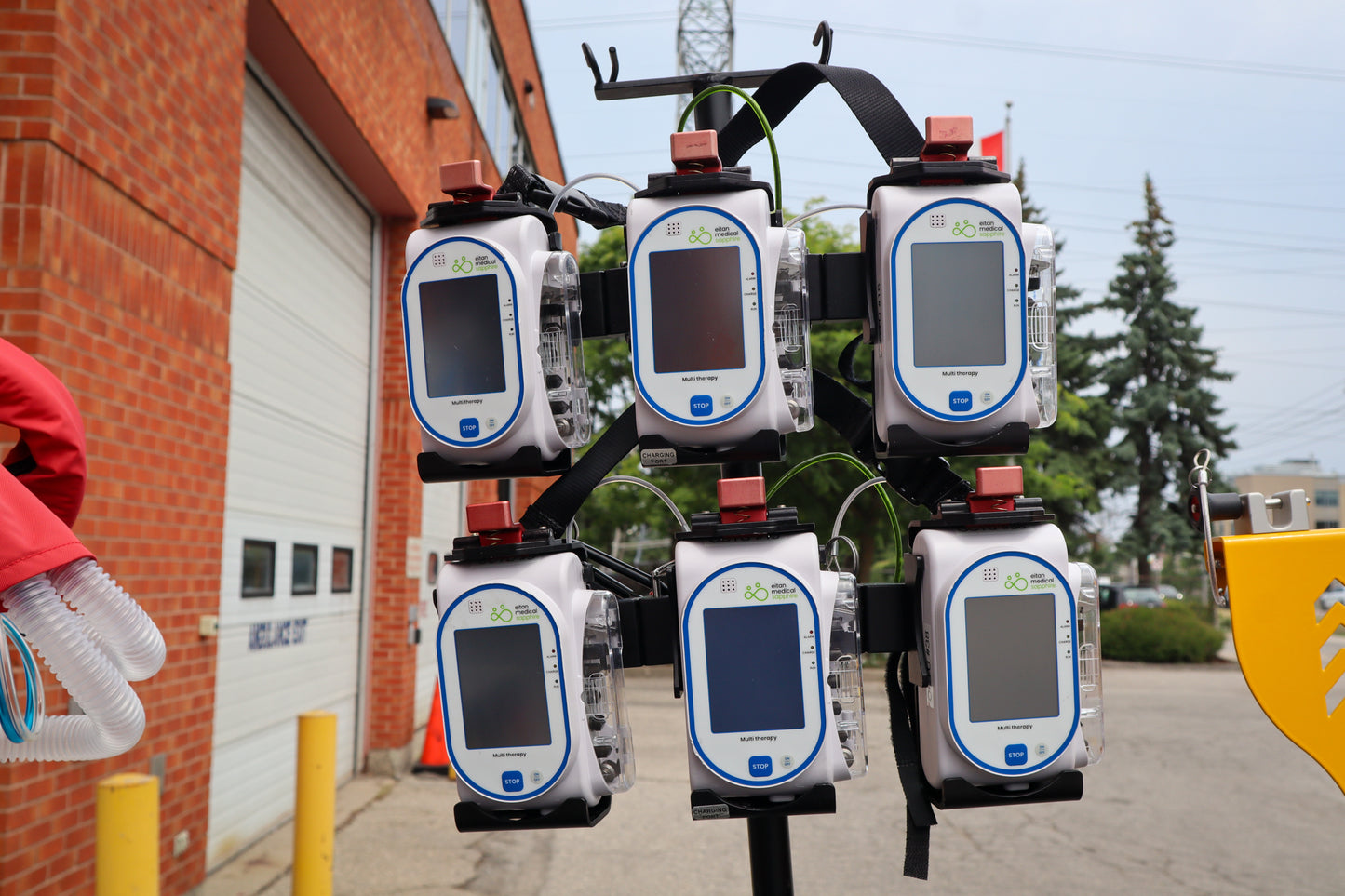 Multiple Sapphire pumps on a Rowland Emergency critical care pole, outdoors with a building and trees in the background.