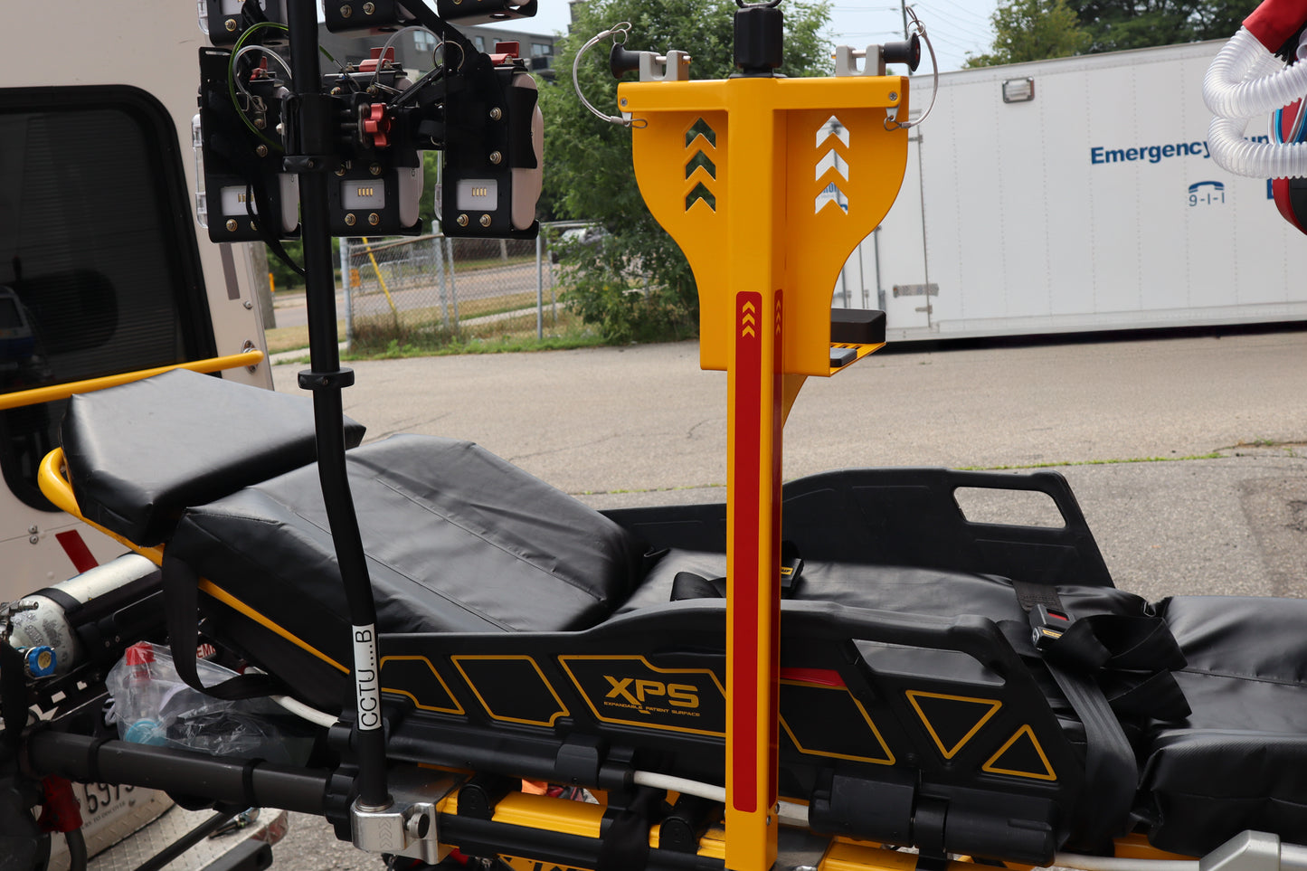 EMT stretcher and Rowland Emergency critical care products with XPS branding on a vehicle, with an Emergency Services truck in the background.