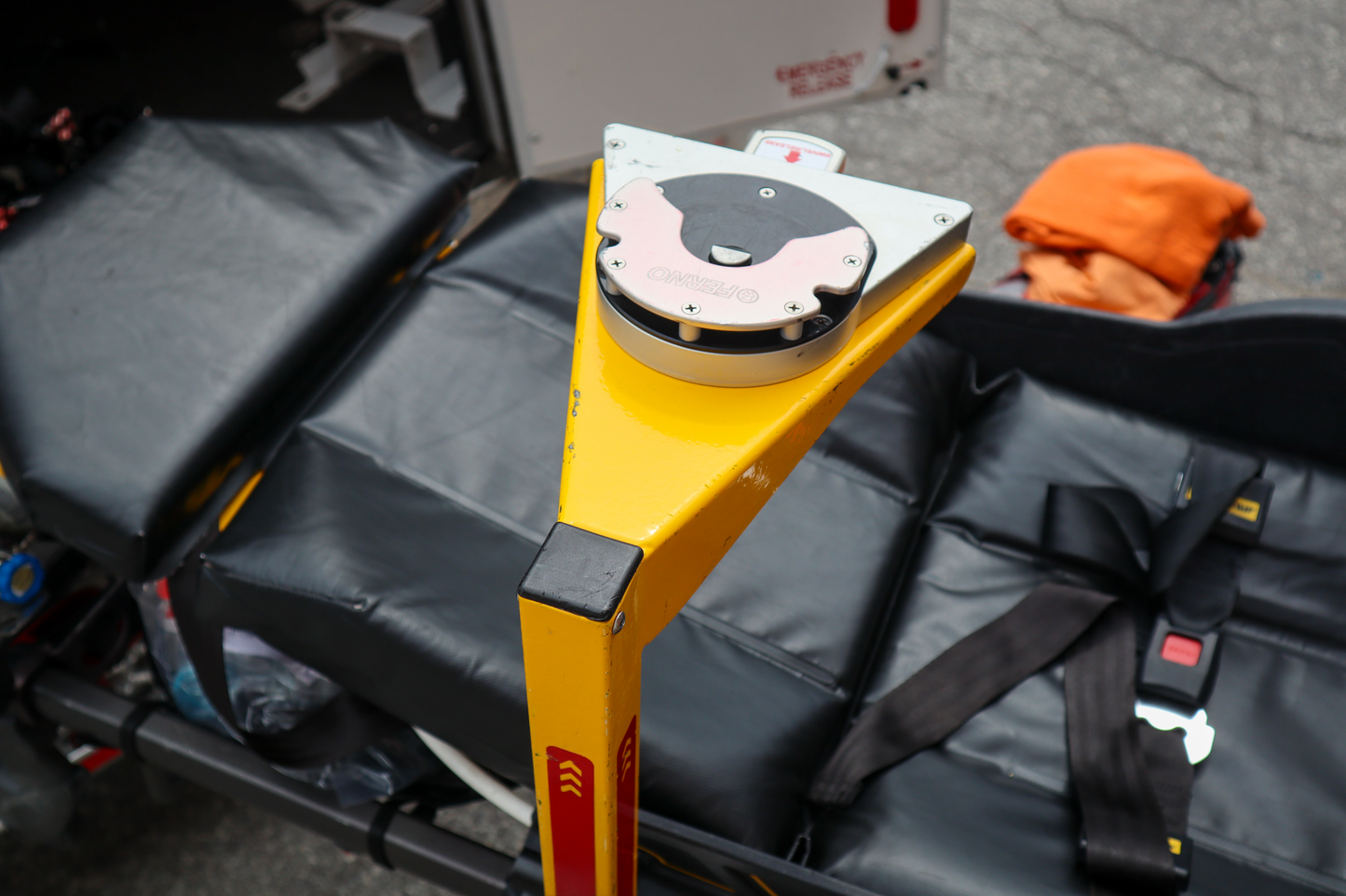 Yellow medical stretcher pole with a Ferno D360 mount on it. Pole is attached to a black stretcher in a parking lot.