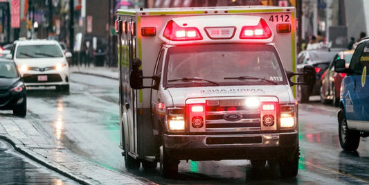 Emergency ambulance with flashing lights driving on wet city street, Rowland Emergency