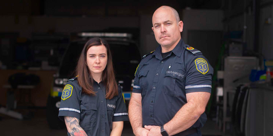 Two Frontenac County paramedics in uniform stand in front of an EMS vehicle in a garage