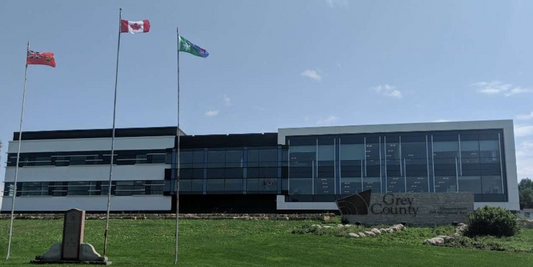 Grey County building with three flags, modern glass exterior, lawn, and Rowland Emergency context