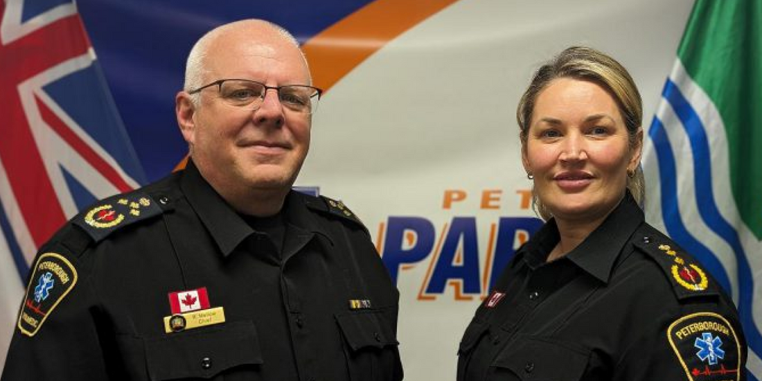 Two Peterborough paramedic chiefs in uniform at Rowland Emergency event, Canada flags in background