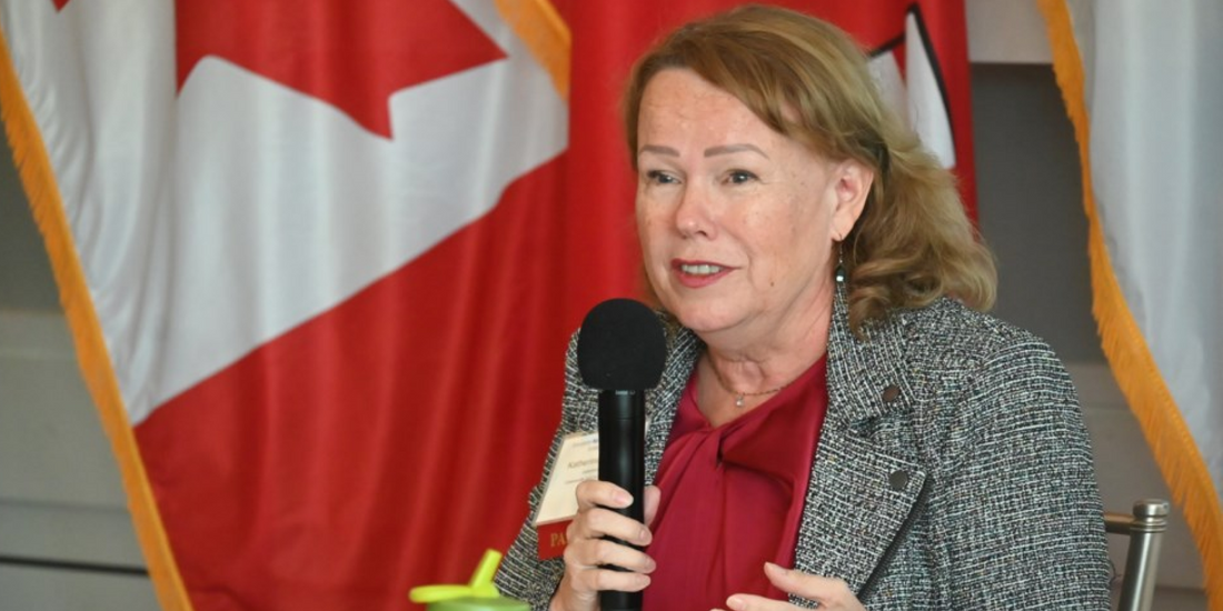 Woman speaking into microphone at emergency preparedness event, Canadian flag in background