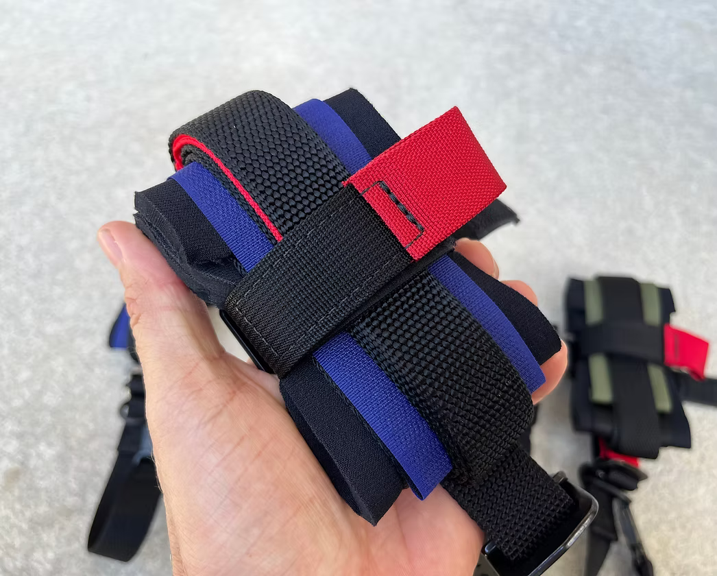 Hand holding a XDcuff REF115C+ black, blue, and red straps on a textured white background