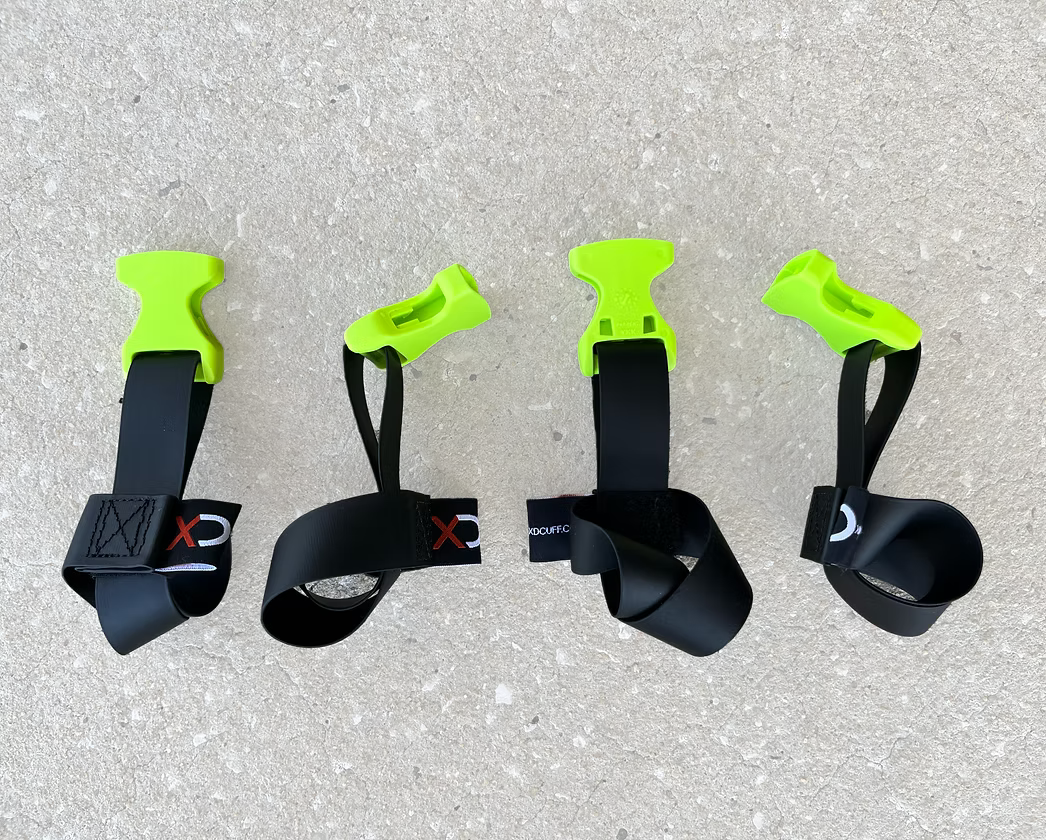 Four XDcuff REF115 black straps with green ends on a concrete surface