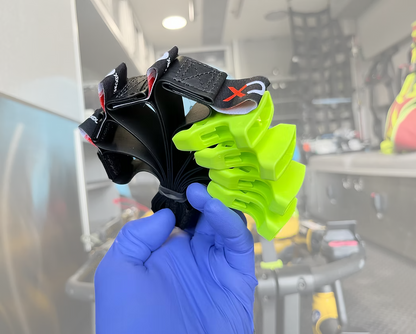 Hand holding a XDcuff REF115 straps (green and black) with a blurred ambulance background