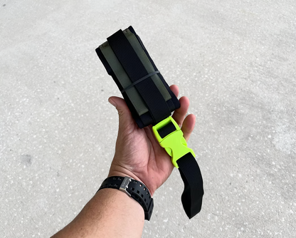Hand holding an XDcuff REF105 black and green strap against a concrete background