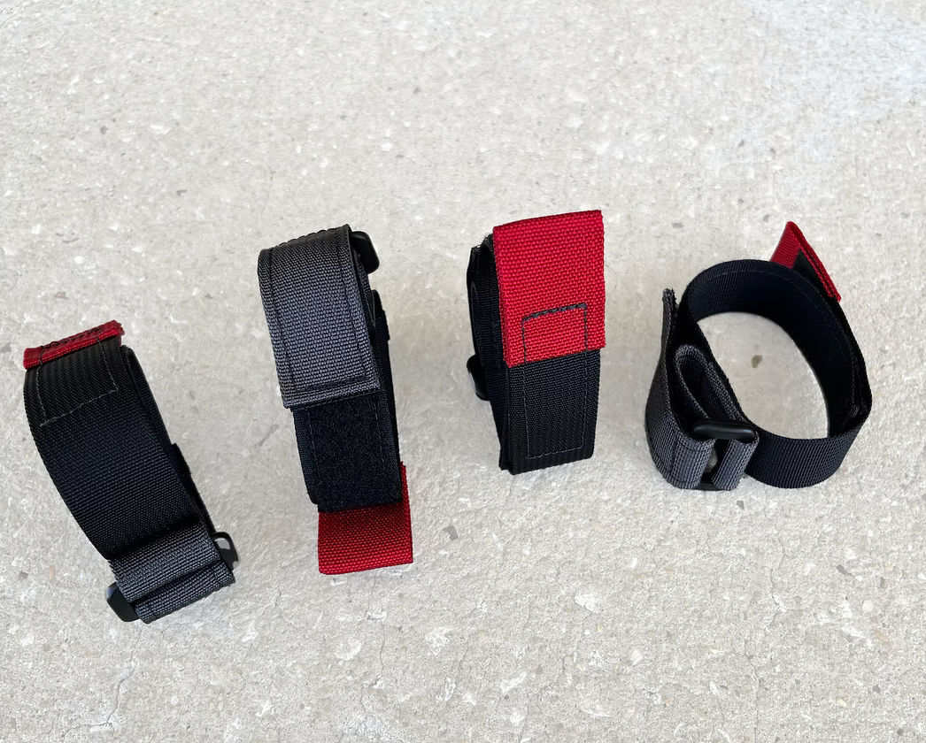 Four black and red XDcuff REF105 straps arranged on a concrete surface