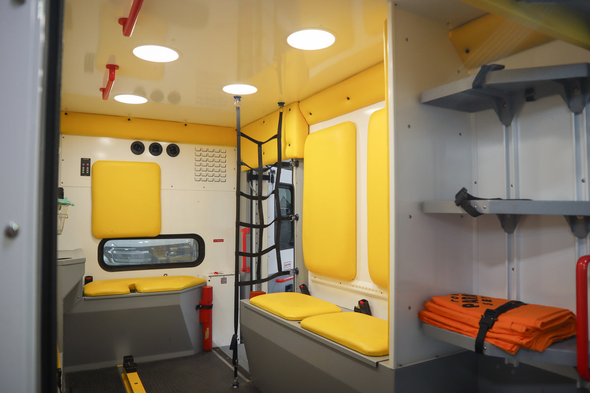 Interior of a medical vehicle with yellow and gray interior, shelves, and emergency equipment.