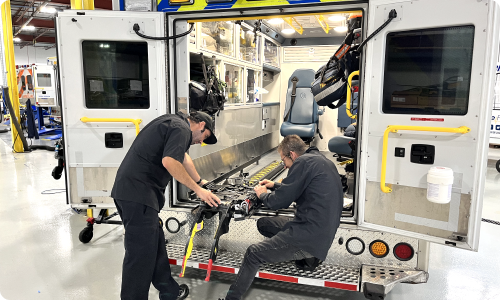 Two Stryker-trained technicians installing and repairing a Stryker Power-LOAD system, ensuring proper functionality and safety for patient transport.